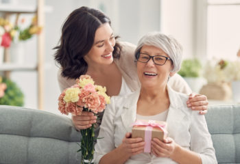 Happy mother's day Happy mother's day! Beautiful young woman and her mother with flowers and gift box at home.
